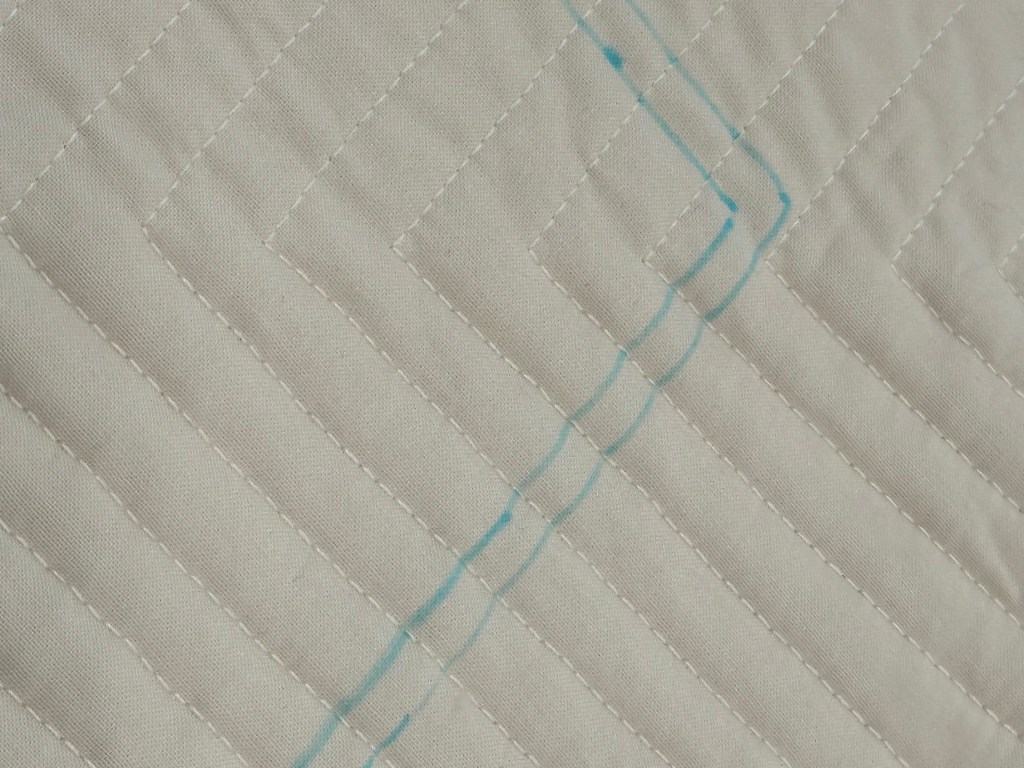 Close-up of a quilted fabric with a zigzag pattern and a blue marking on a cream background.