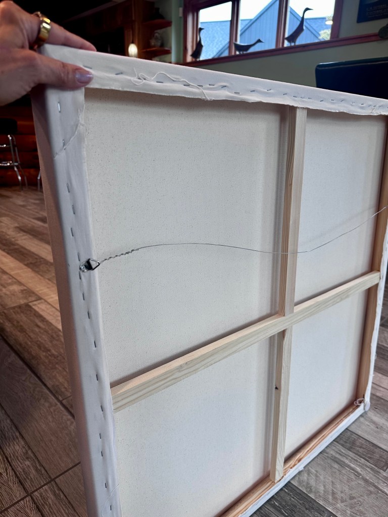A close-up view of the back of an unframed canvas, showing the wooden stretcher bars and the stitching along the edges, with visible creases and a slight tear.